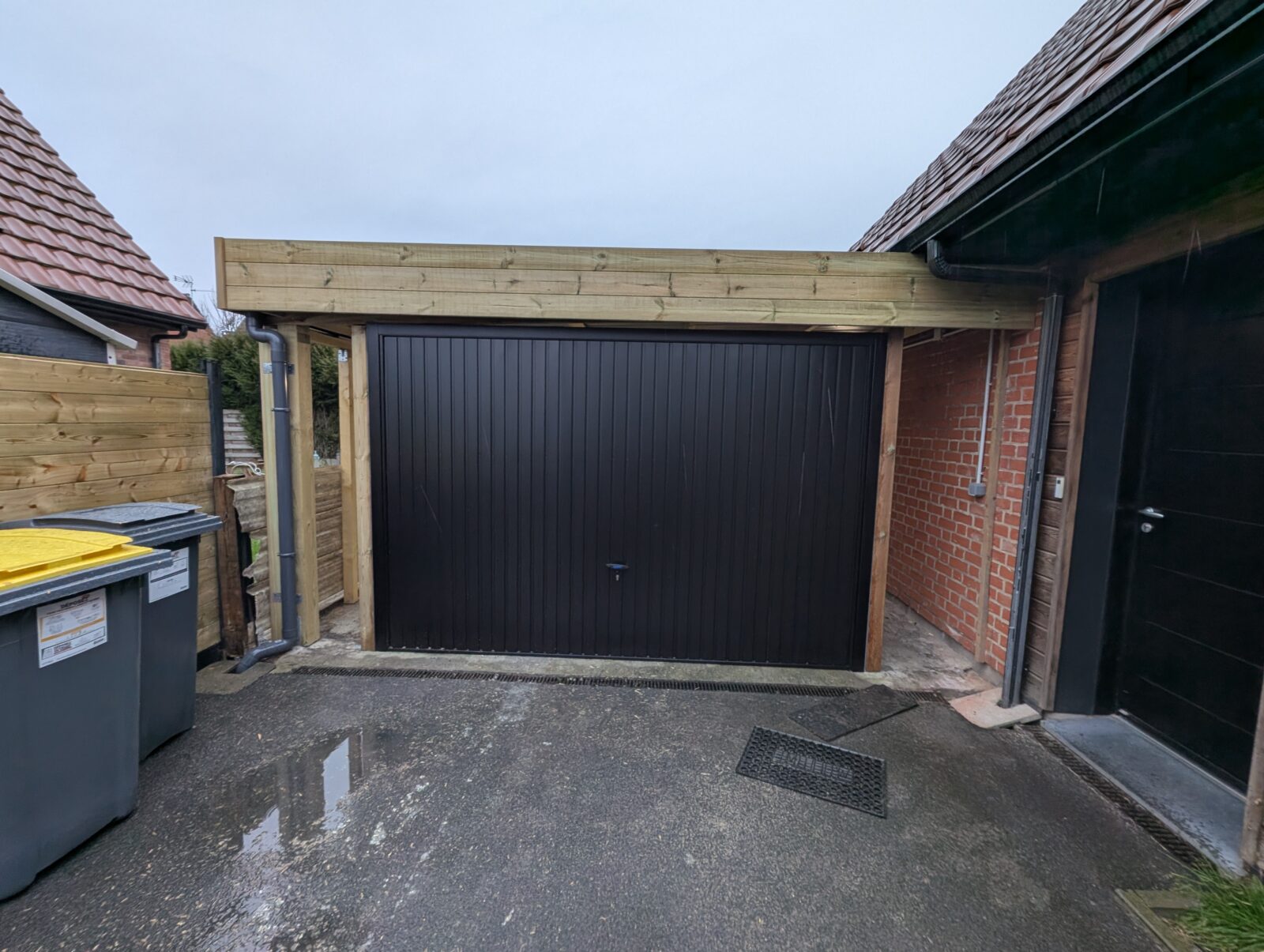Vue extérieure d'un porte de garage basculante noire de marque Novoferm posée sur carport existant en bois à Neuville en Ferrain (Nord) .jpg