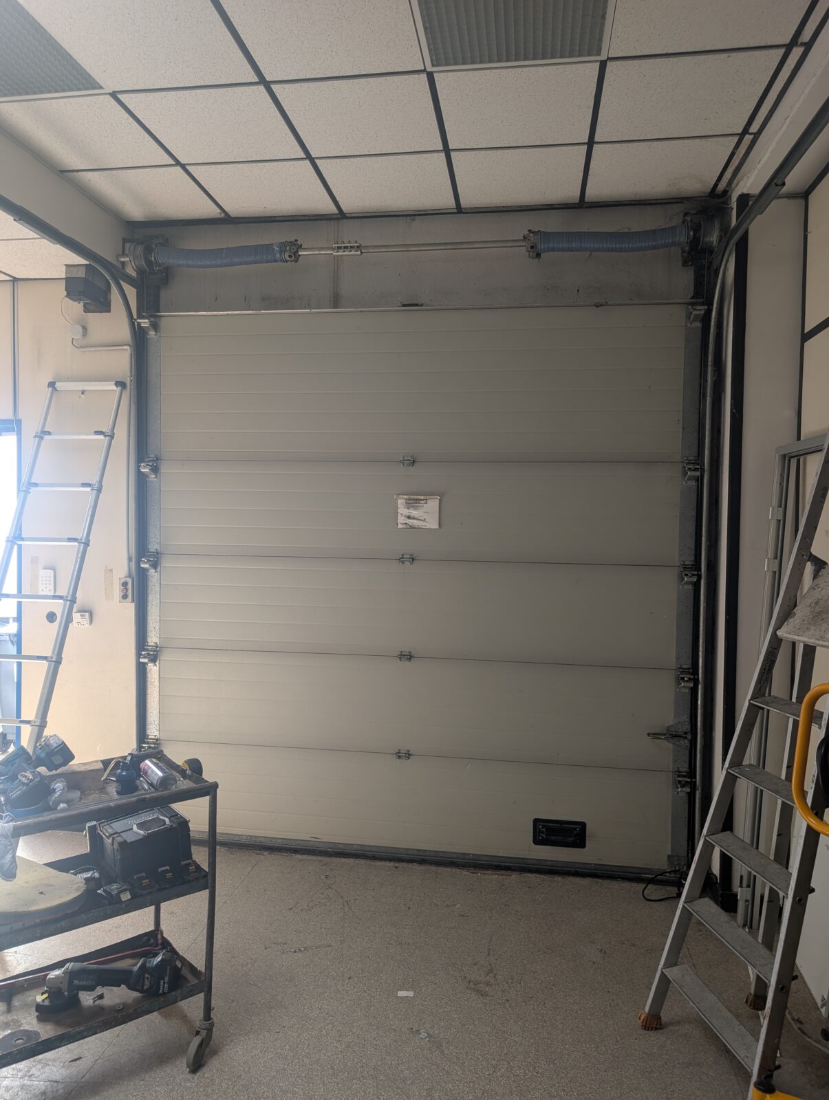 Dépannage et réparation d'une porte sectionnelle, changement des ressors de tension ainsi que des câbles de traction suivi d'un entretien pour une utilisation optimale d'une porte d'entrepôts à Frelinghien (59).