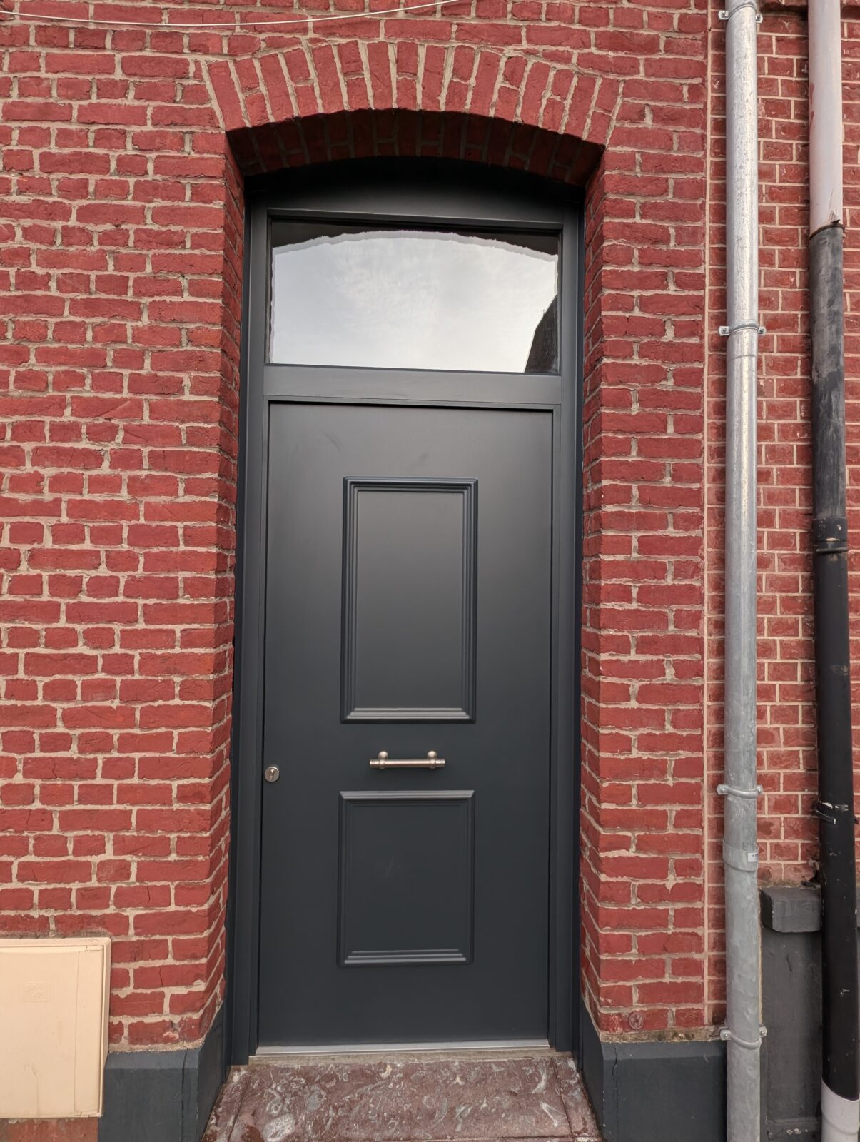 Porte d’entrée noire à panneaux moulurés dans une façade en briques rouges à Roubaix (59).